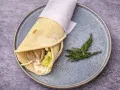 Pita co to? Sycący wrap z mięsem, warzywami i sosem, zawinięty w płaski chlebek, podany na talerzu z gałązką koperku.