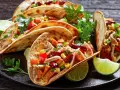 Pyszne meksykańskie jedzenie: tacos z kurczakiem, fasolą, kukurydzą i papryką, podane z limonką i kolendrą.
