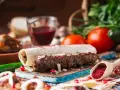 Pyszny gruziński kebab zawinięty w lawasz, posypany sumakiem i ziołami, z dodatkami warzyw i sosu.