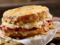 Pyszny croque madame z rozpływającym się serem i szynką, podany na papierze na drewnianej desce.