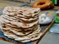 Stos świeżego, ciepłego ciasta na kebab, obok miseczka jajek i okrągły chleb.