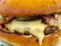 Pyszny burger z dzika z rozpływającym się serem, chrupiącym boczkiem i piklami. Idealny na leśną ucztę!