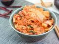 Misternie przygotowane kimchi, czyli co to jest? Pikantna, fermentowana kapusta pekińska w misce, obok pałeczki i suszone papryczki chili.