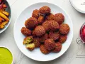 Talerz pełen chrupiących kulek falafela, które są smażonymi kotlecikami z ciecierzycy. Obok frytki i zielony sos.