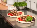 Ręce w rękawiczkach układają mięso na plackach z pomidorami i zieloną sałatą. Pyszny kebab gemuse gotowy do podania.