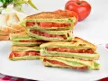 Pyszne włoskie kanapki z pomidorami i zielonym pesto, ułożone na talerzu. Idealne na lekki posiłek.