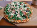 Pyszna pizza z rukolą, oliwkami, parmezanem i cienkimi plastrami prosciutto.