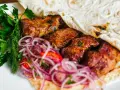Pyszne mezze: soczyste mięso zawinięte w placek, z dodatkiem świeżej natki i czerwonej cebuli. Idealne na przekąskę.