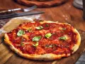 Pikantna spianata calabrese na pizzy, ozdobiona świeżą bazylią i ziołami, czeka na talerzu.