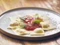 Pyszne raviolini z sosem pomidorowym i parmezanem, ozdobione listkami szałwii, na szarym talerzu.