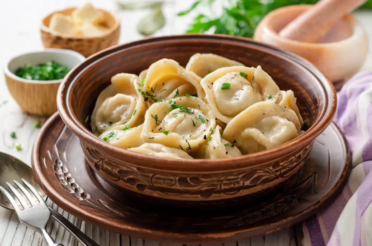Pielmieni co to? Pyszne, domowe pierożki z mięsem, posypane świeżym koperkiem, w glinianej misce.