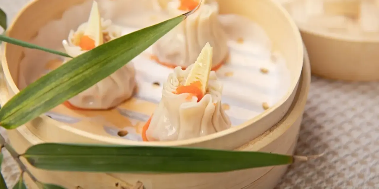Pierożki dim sum w bambusowym parowniku, ozdobione kawałkiem bambusa i pomarańczowym ikrą.