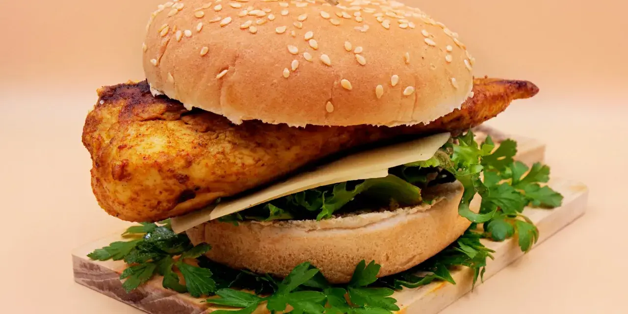 Pikantny kurczakburger z serem i świeżą sałatą, podany na desce z natką pietruszki.