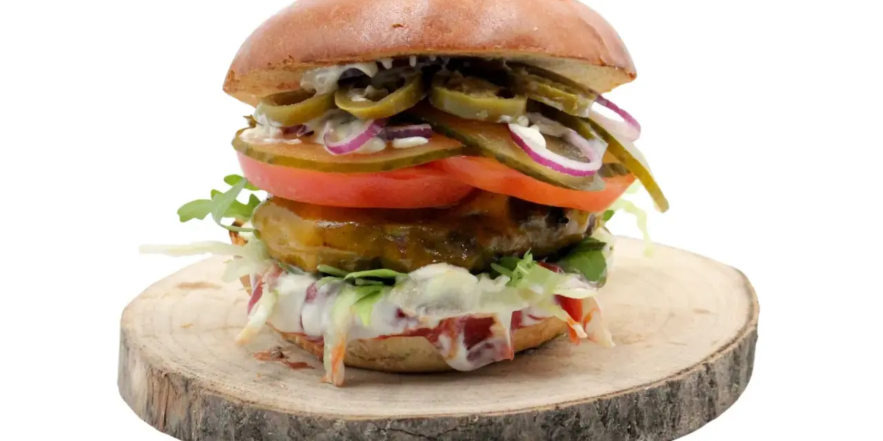 Pikantny jalapeno burger z pomidorem, cebulą i sałatą na drewnianym krążku. Zastanawiasz się nad jego kcal?