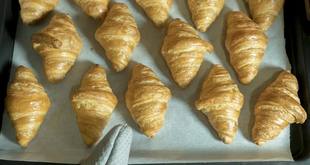 Pyszne, złociste croissanty ułożone na blasze. Idealne na śniadanie.