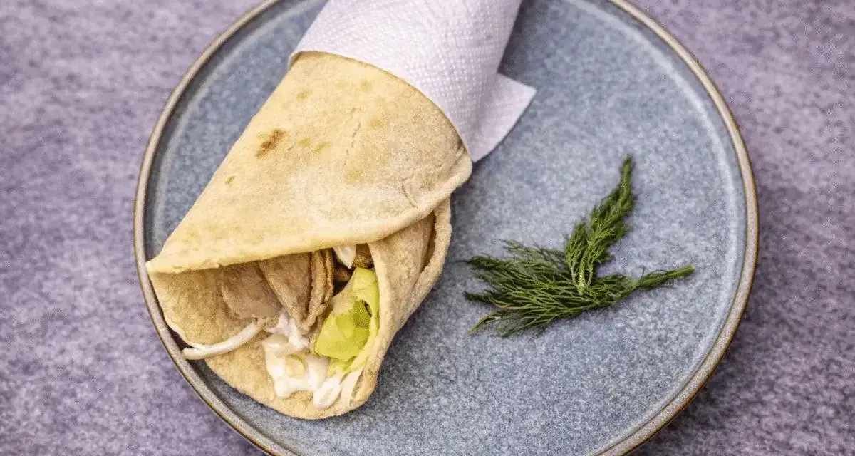 Pita co to? Sycący wrap z mięsem, warzywami i sosem, zawinięty w płaski chlebek, podany na talerzu z gałązką koperku.