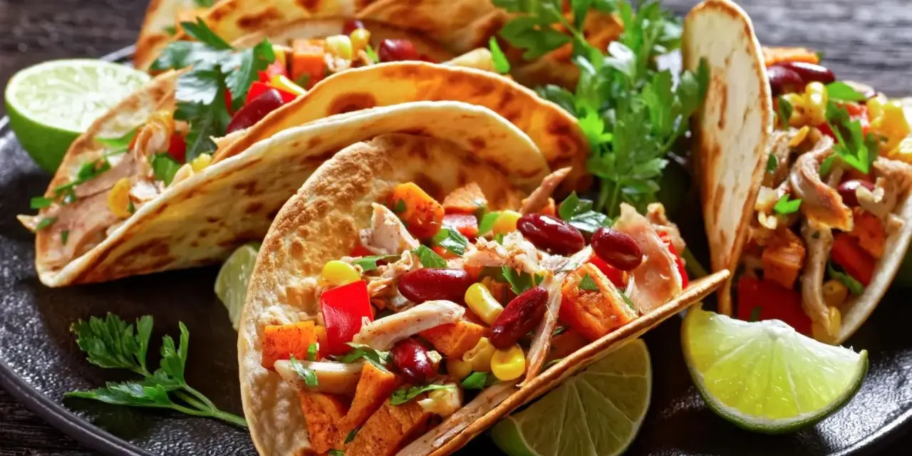 Pyszne meksykańskie jedzenie: tacos z kurczakiem, fasolą, kukurydzą i papryką, podane z limonką i kolendrą.
