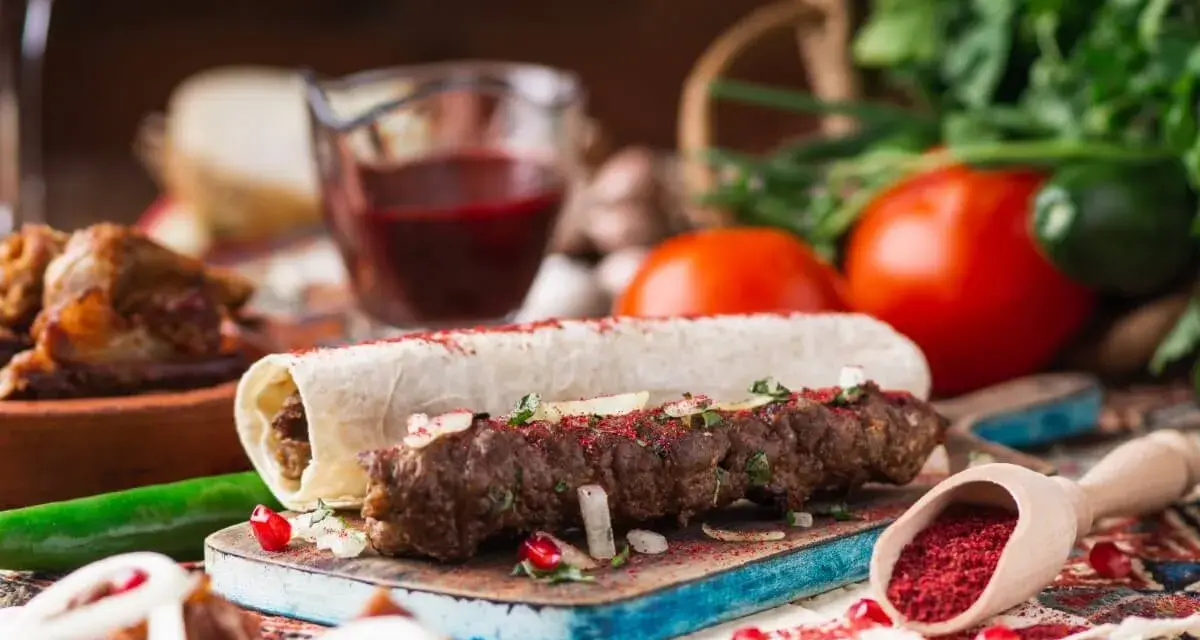 Pyszny gruziński kebab zawinięty w lawasz, posypany sumakiem i ziołami, z dodatkami warzyw i sosu.