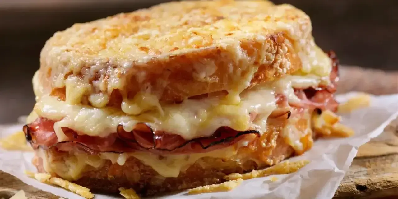 Pyszny croque madame z rozpływającym się serem i szynką, podany na papierze na drewnianej desce.