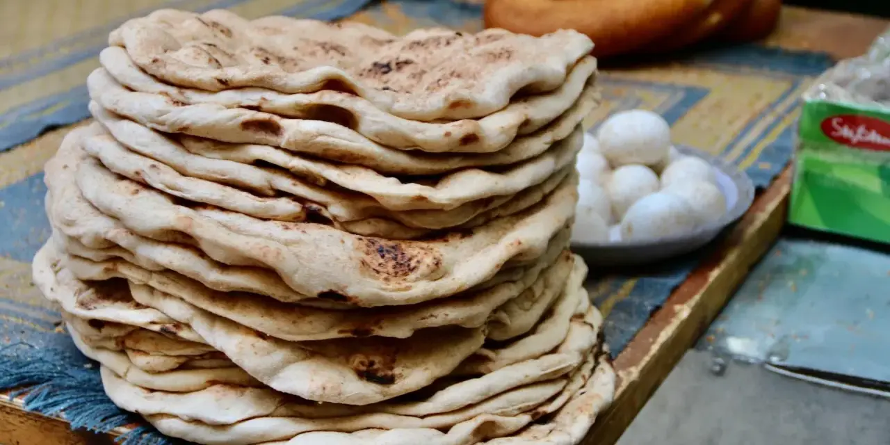Stos świeżego, ciepłego ciasta na kebab, obok miseczka jajek i okrągły chleb.