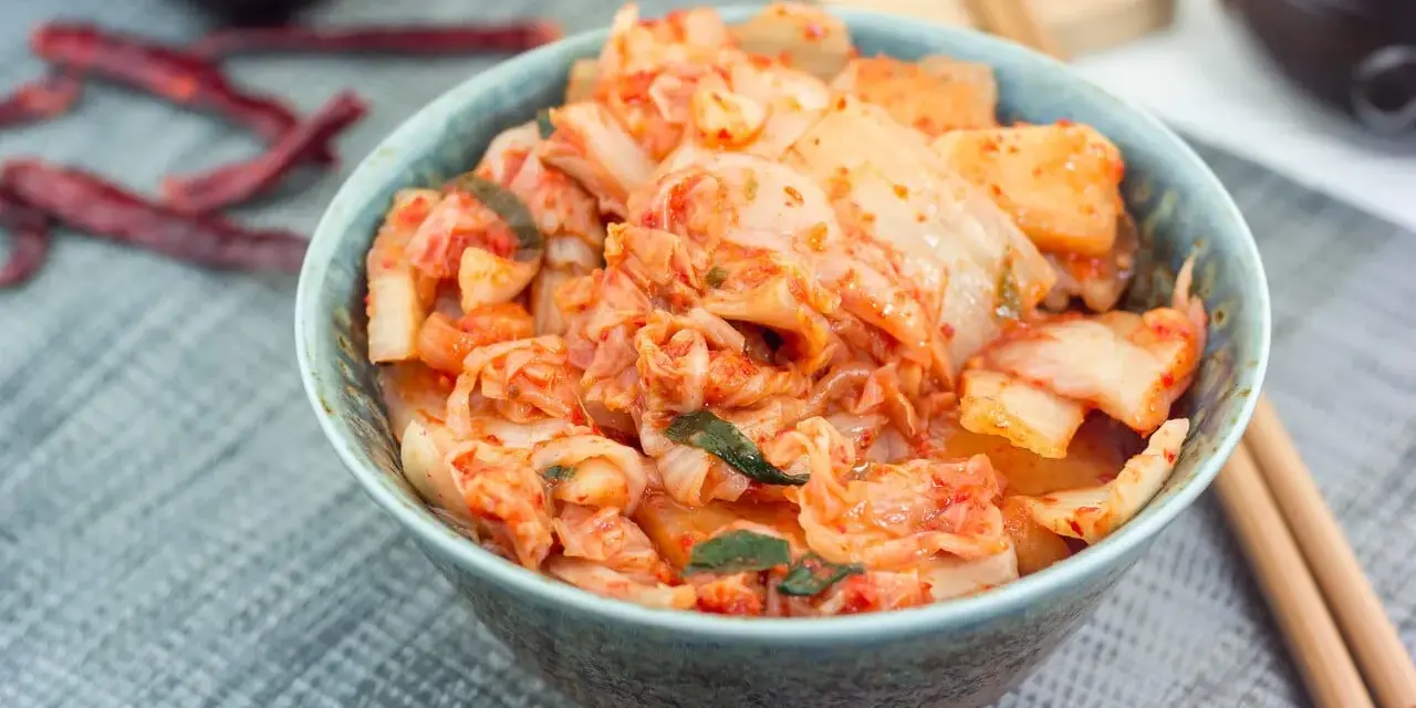 Misternie przygotowane kimchi, czyli co to jest? Pikantna, fermentowana kapusta pekińska w misce, obok pałeczki i suszone papryczki chili.