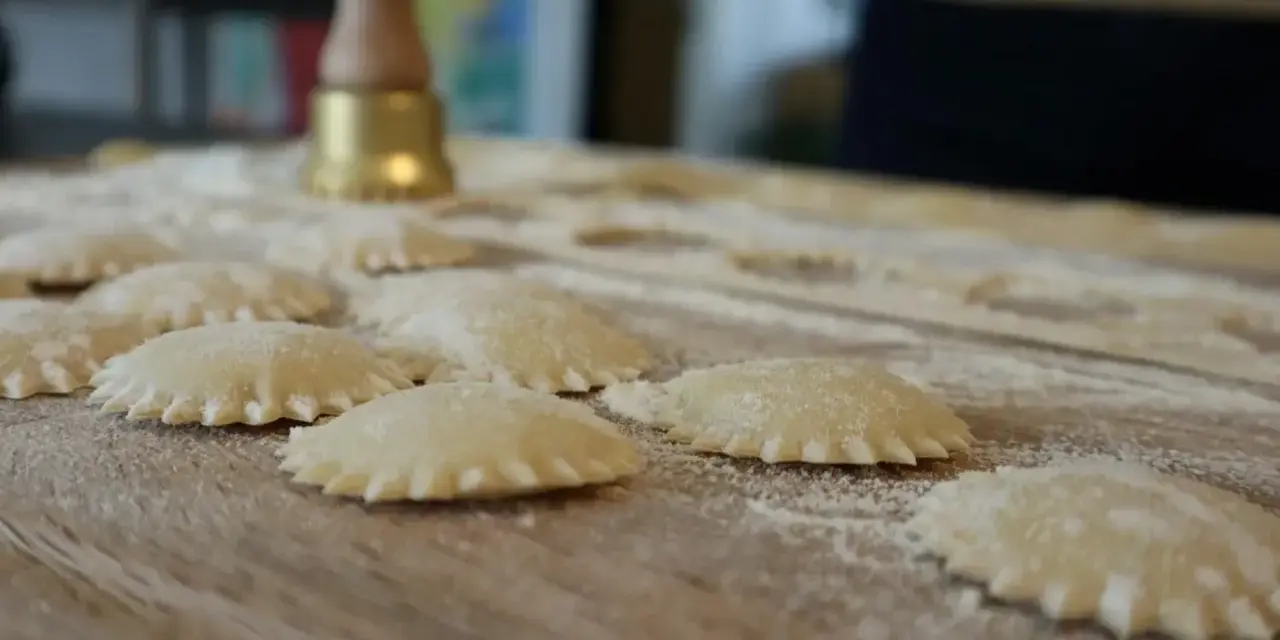 Świeże ravioli na drewnianej desce, posypane mąką. Zastanawiasz się, ravioli z czym podawać?