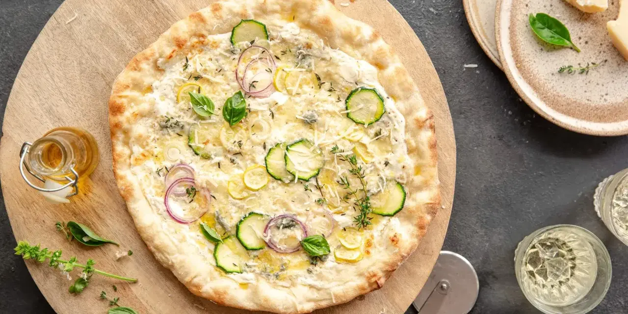 Pyszna pizza bianca z cukinią, cebulą i cytryną, posypana parmezanem i ziołami. Idealna na letni wieczór.