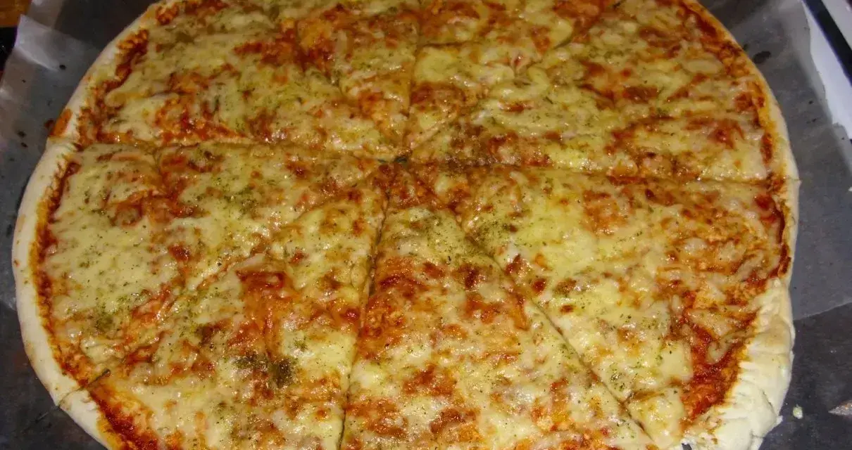Pyszna pizza margerita z ciągnącym się serem i aromatycznymi ziołami, pokrojona na 8 kawałków.