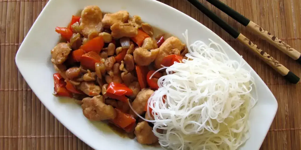 Kurczak kung pao po seczuańsku z orzeszkami ziemnymi i papryką, podany z ryżowym makaronem.