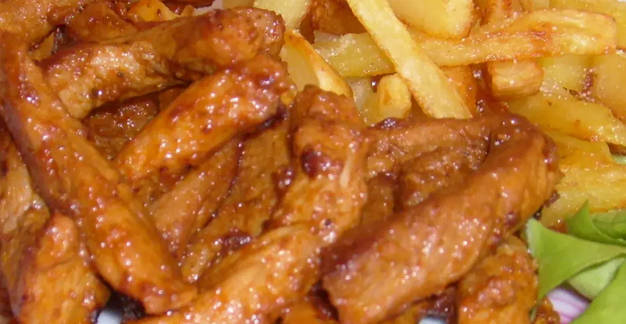 Pyszny gyros wieprzowy w sosie, podany z chrupiącymi frytkami i świeżą sałatą. Idealny posiłek dla każdego miłośnika mięsa.