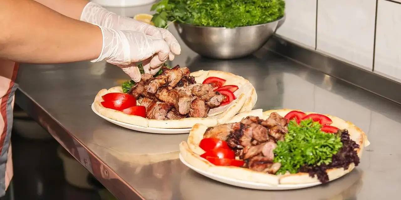 Ręce w rękawiczkach układają mięso na plackach z pomidorami i zieloną sałatą. Pyszny kebab gemuse gotowy do podania.