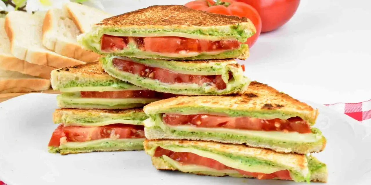 Pyszne włoskie kanapki z pomidorami i zielonym pesto, ułożone na talerzu. Idealne na lekki posiłek.