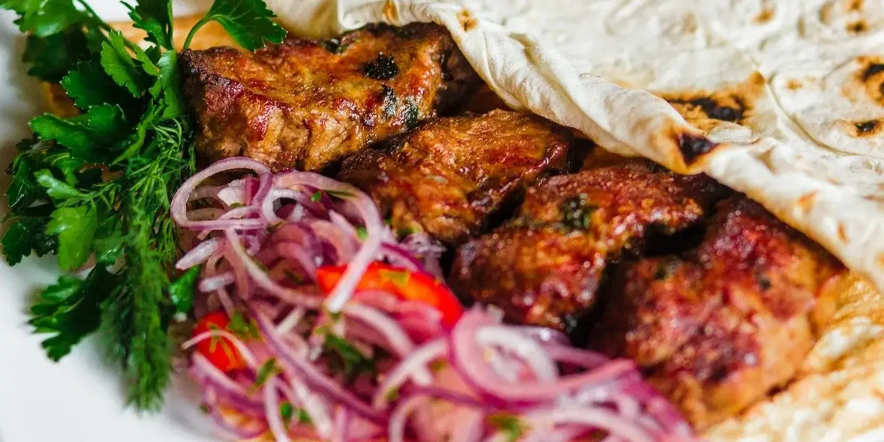 Pyszne mezze: soczyste mięso zawinięte w placek, z dodatkiem świeżej natki i czerwonej cebuli. Idealne na przekąskę.