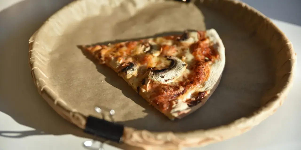 Kawałek pizzy z pieczarkami na papierowym talerzu. Zastanawiasz się, ile kalorii ma pizza?