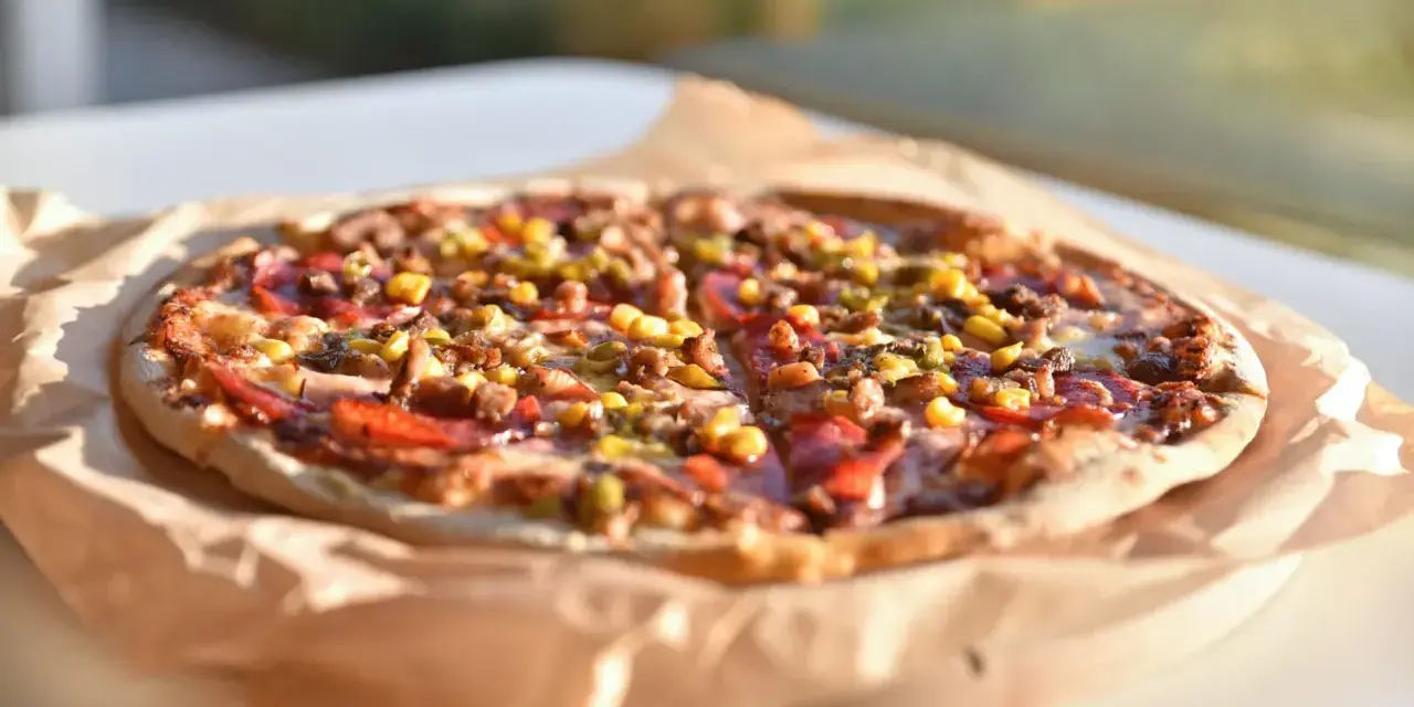 Apetyczna pizza Guiseppe 4 sery, z widocznymi kawałkami mięsa, kukurydzy i papryki, leży na papierze do pieczenia.