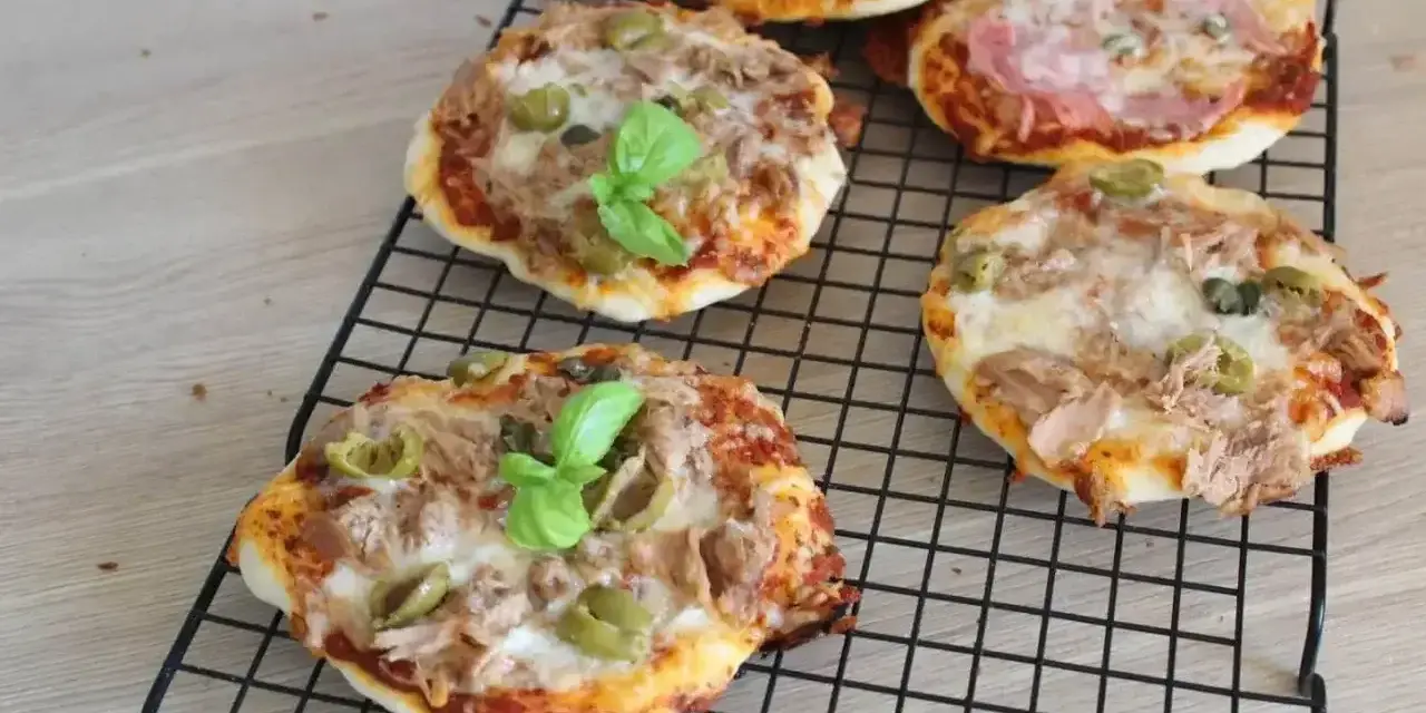 Kilka pysznych pizzett z tuńczykiem, oliwkami i bazylią na czarnej kratce.
