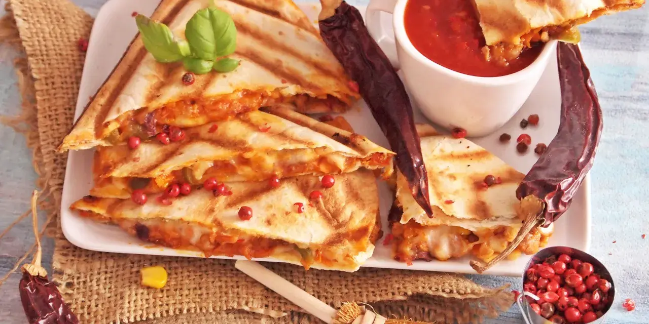 Pyszna quesadilla z serem i papryczkami chili, podana z sosem pomidorowym i ziarnami pieprzu.