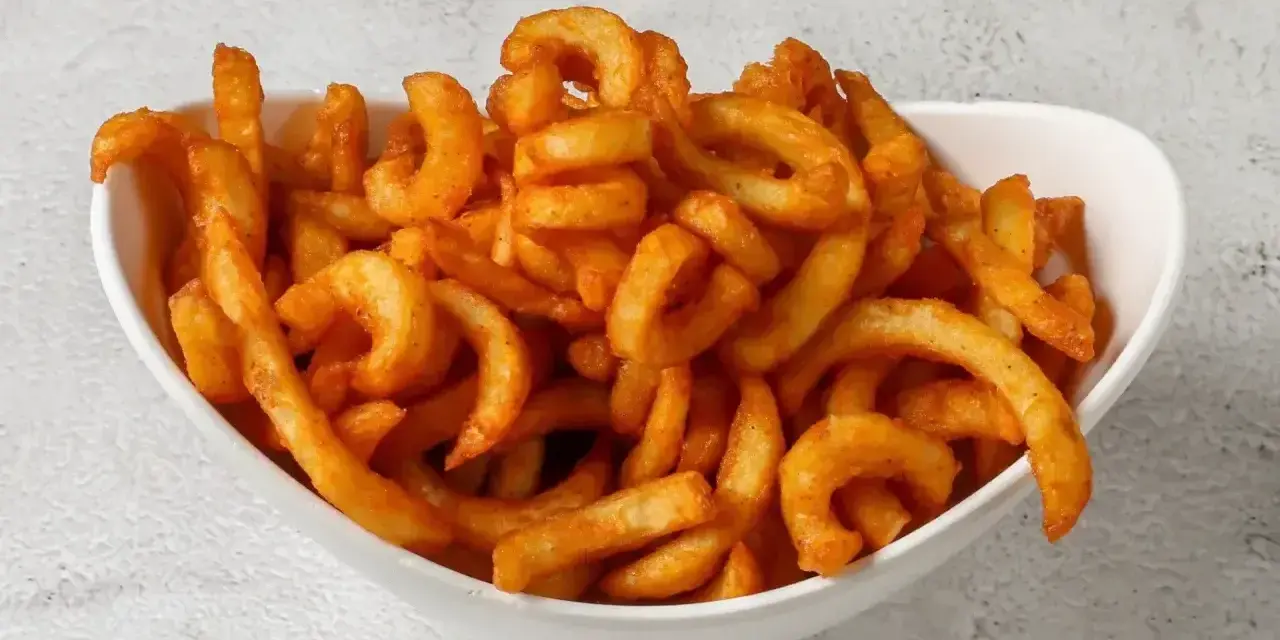Miseczka pełna kręconych frytek creole, posypanych przyprawami.