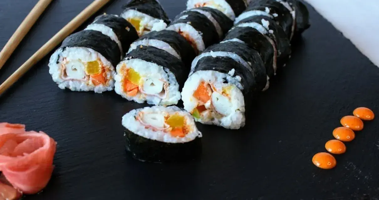 Rząd hosomaki surimi z marchewką i żółtą papryką, podane z imbirem i pomarańczowym sosem.
