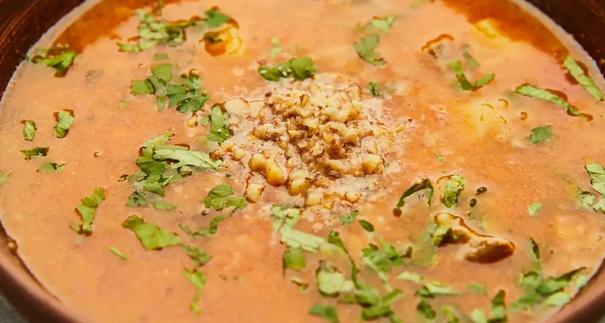 Aromatic gruzińska zupa charczo w glinianej misce, ozdobiona posiekanymi orzechami i świeżą kolendrą.