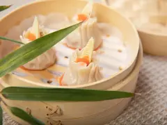 Pierożki dim sum w bambusowym parowniku, ozdobione kawałkiem bambusa i pomarańczowym ikrą.