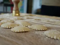 Świeże ravioli na drewnianej desce, posypane mąką. Zastanawiasz się, ravioli z czym podawać?