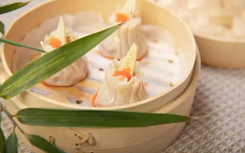 Pierożki dim sum w bambusowym parowniku, ozdobione kawałkiem bambusa i pomarańczowym ikrą.