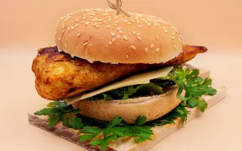 Pikantny kurczakburger z serem i świeżą sałatą, podany na desce z natką pietruszki.