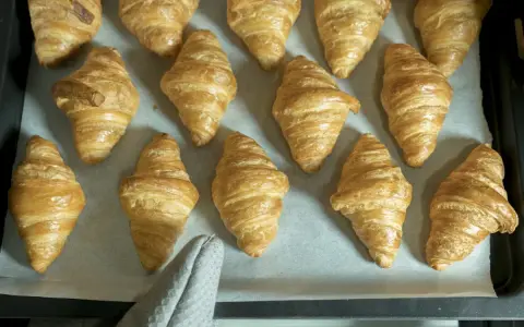 Pyszne, złociste croissanty ułożone na blasze. Idealne na śniadanie.