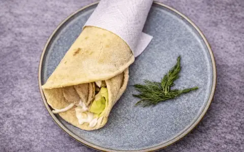 Pita co to? Sycący wrap z mięsem, warzywami i sosem, zawinięty w płaski chlebek, podany na talerzu z gałązką koperku.