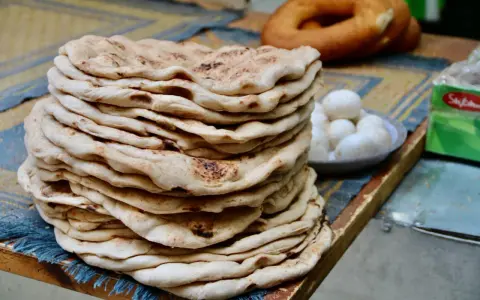 Stos świeżego, ciepłego ciasta na kebab, obok miseczka jajek i okrągły chleb.