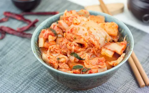 Misternie przygotowane kimchi, czyli co to jest? Pikantna, fermentowana kapusta pekińska w misce, obok pałeczki i suszone papryczki chili.