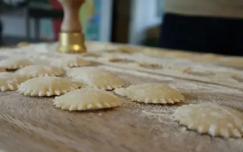 Świeże ravioli na drewnianej desce, posypane mąką. Zastanawiasz się, ravioli z czym podawać?