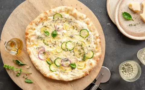Pyszna pizza bianca z cukinią, cebulą i cytryną, posypana parmezanem i ziołami. Idealna na letni wieczór.